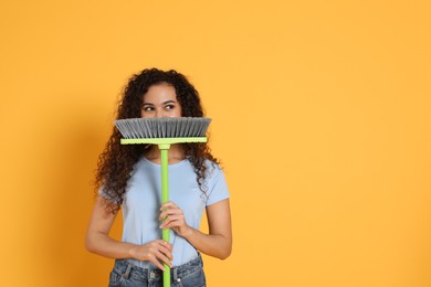 African American woman with green broom on orange background, space for text