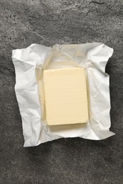 Photo of Block of tasty butter in open foil packaging on grey table, top view