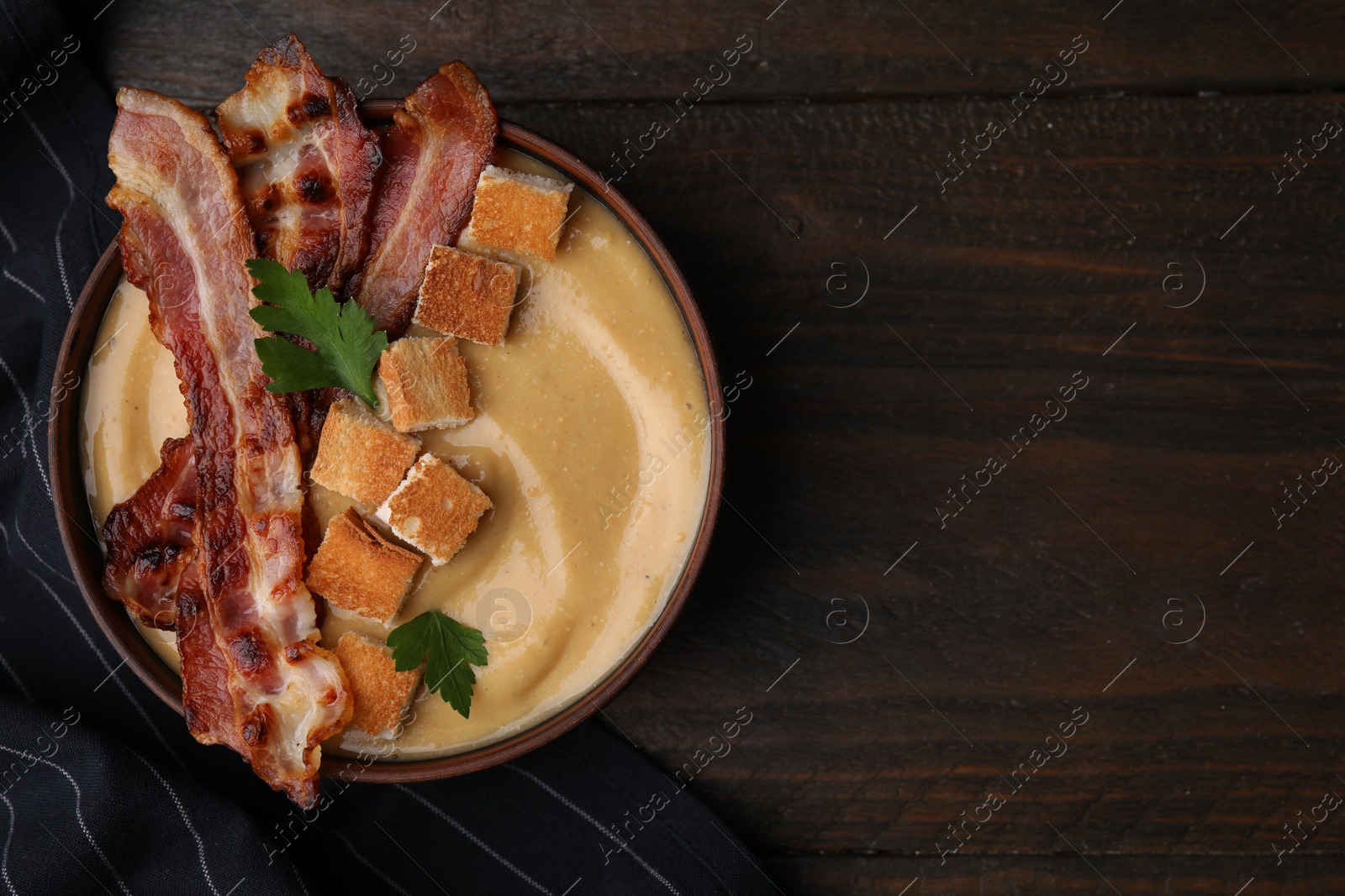 Photo of Delicious lentil soup with bacon and parsley in bowl on wooden table, top view. Space for text