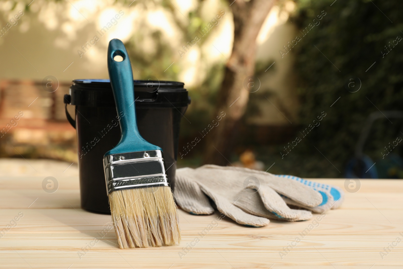 Photo of Bucket with varnish, brush and gloves on wooden table. Space for text