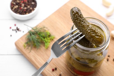 Photo of Fork with tasty pickled cucumber near jar on table, closeup