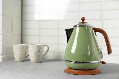 Photo of Stylish electric kettle and tea cups on grey table against white wall