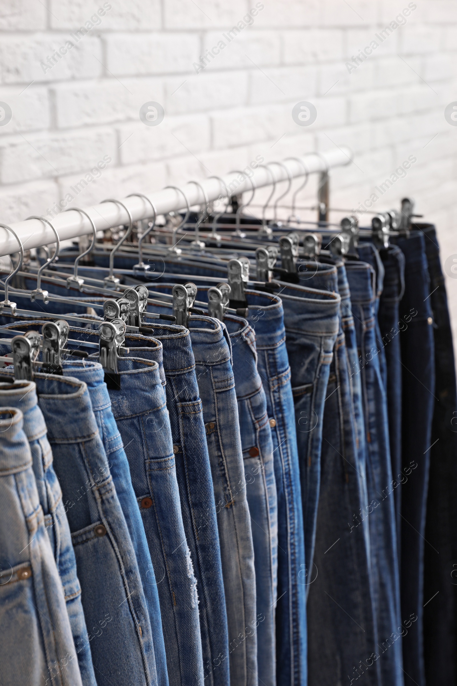 Photo of Rack with stylish jeans near brick wall, closeup