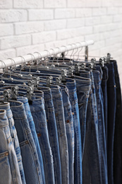 Rack with stylish jeans near brick wall, closeup