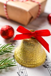 Photo of Golden shiny bell with red bow and music sheet on table, closeup. Christmas decoration