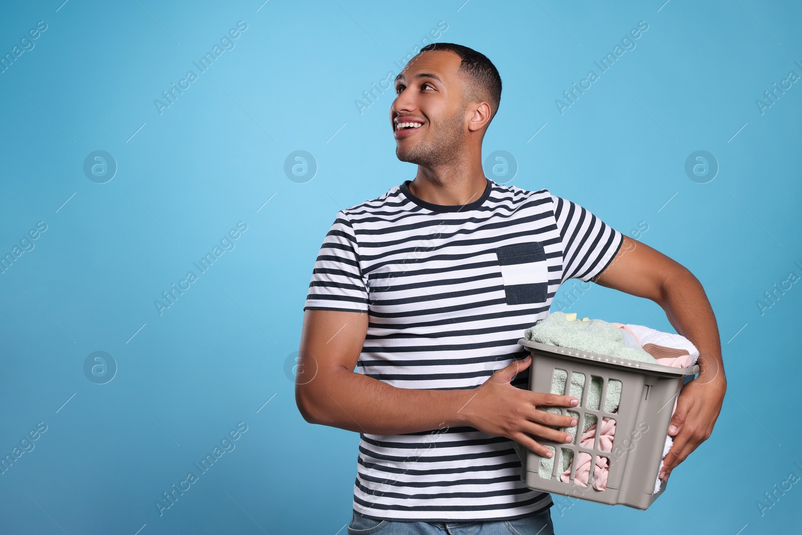 Photo of Happy man with basket full of laundry on light blue background