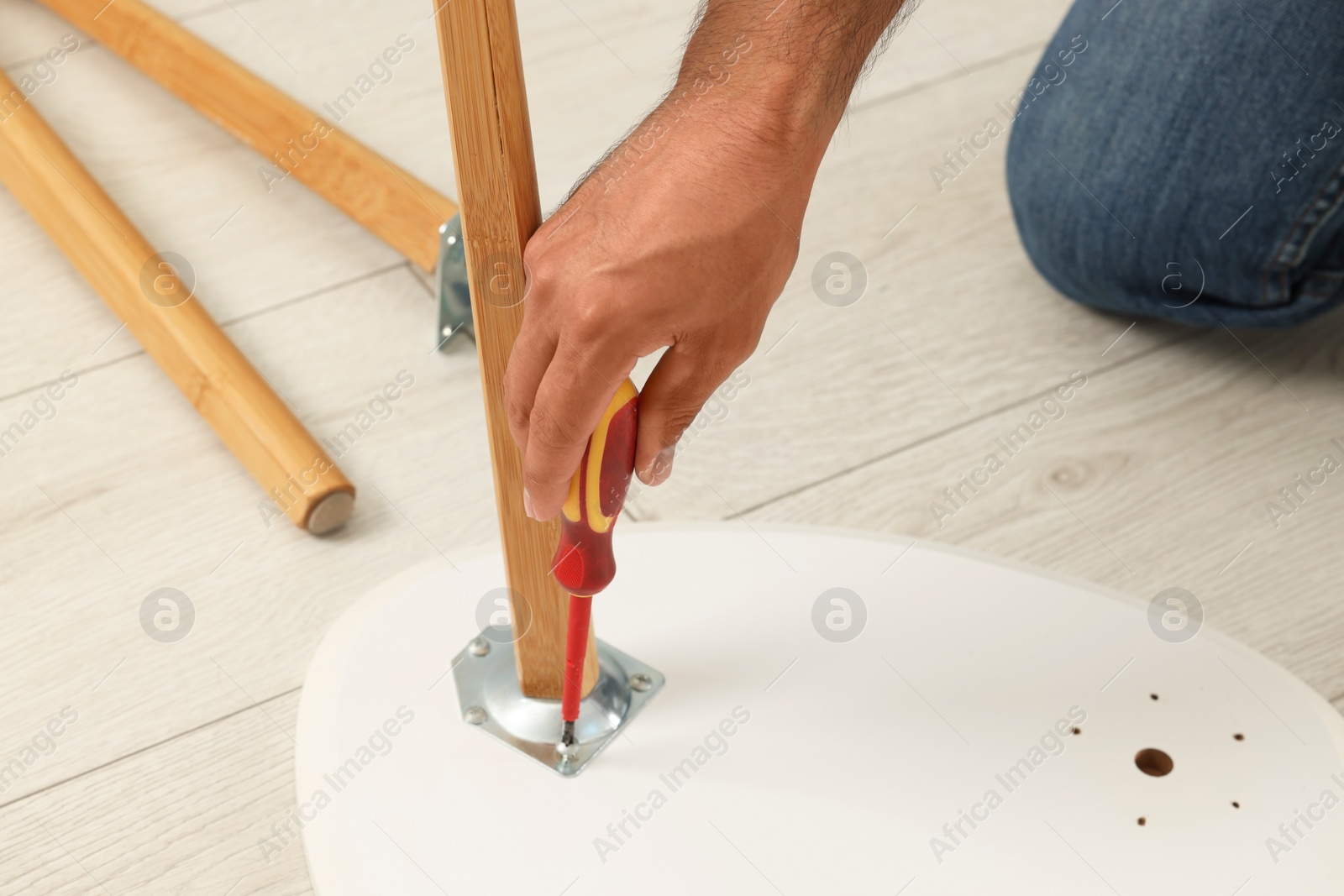 Photo of Man with screwdriver assembling furniture on floor, closeup