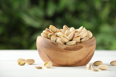 Photo of Tasty pistachios in bowl on white table against blurred background