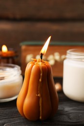 Burning candle in shape of pumpkin on wooden table, closeup. Autumn atmosphere