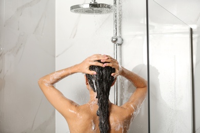 Young woman washing hair in shower at home, back view