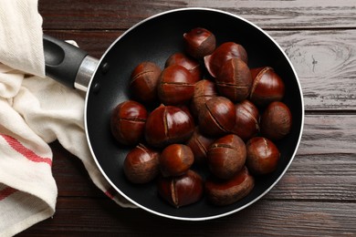 Photo of Roasted edible sweet chestnuts in frying pan on wooden table, top view