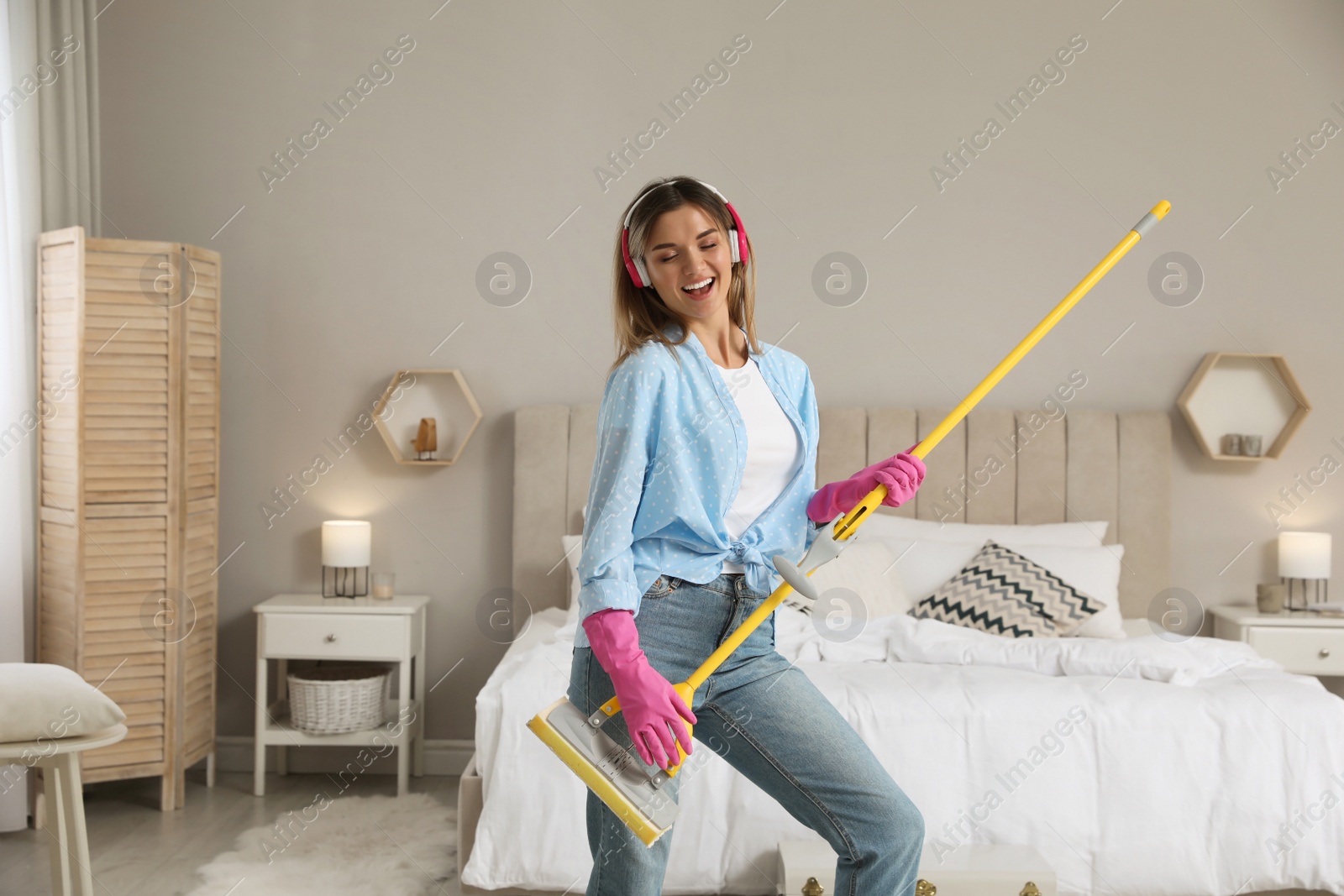 Photo of Woman in headphones with mop singing while cleaning at home