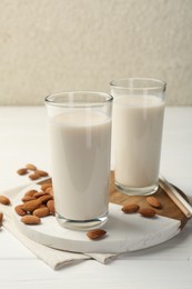 Glasses of almond milk and almonds on white wooden table