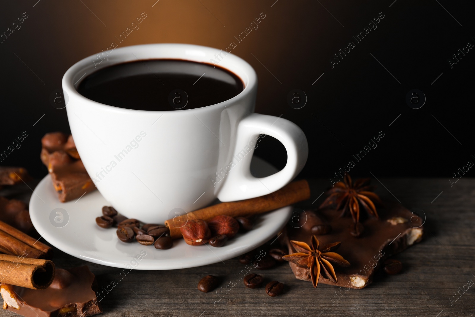 Photo of Cup of delicious hot chocolate, spices and coffee beans on wooden table