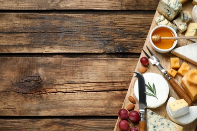 Photo of Cheese platter with specialized knife and fork on wooden table, flat lay. Space for text