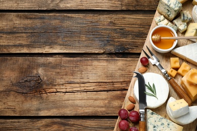 Cheese platter with specialized knife and fork on wooden table, flat lay. Space for text