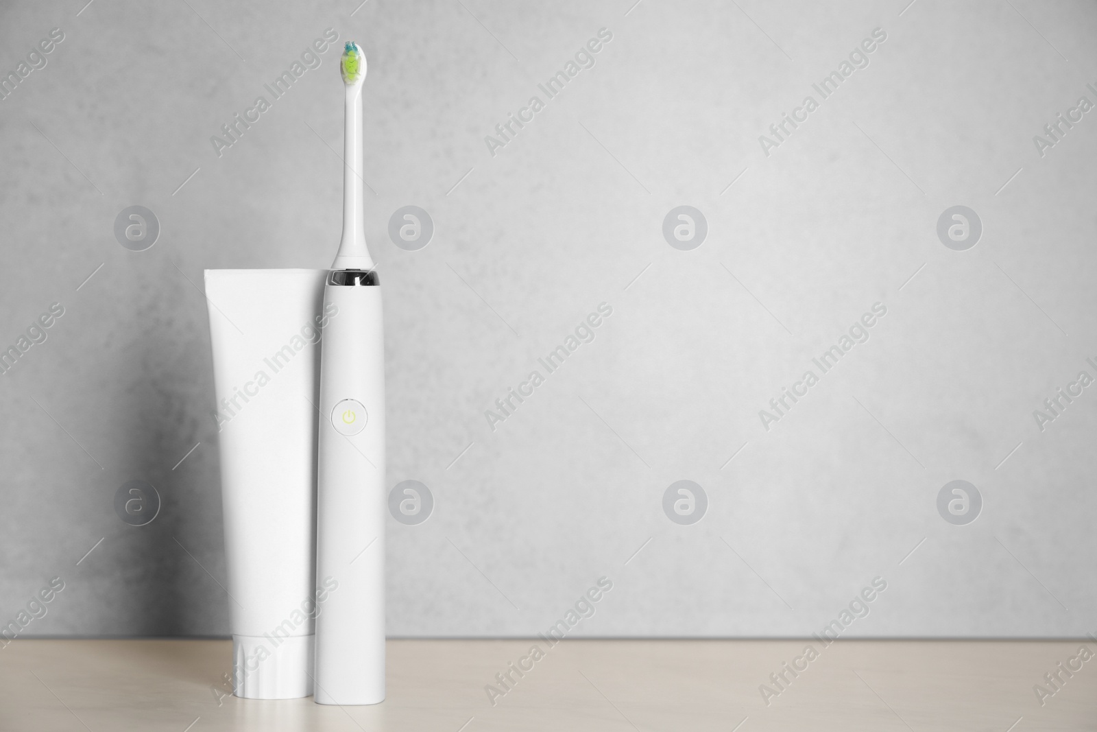 Photo of Electric toothbrush and toothpaste on light background, space for text