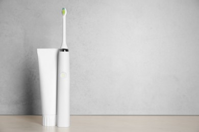 Electric toothbrush and toothpaste on light background, space for text