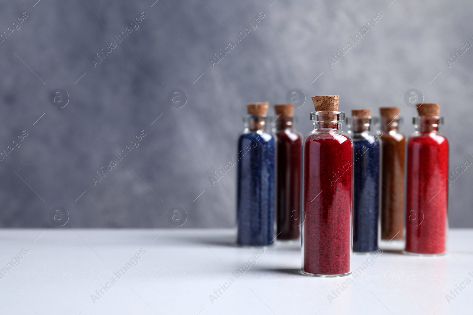 Photo of Glass bottles with different food coloring on white marble table. Space for text