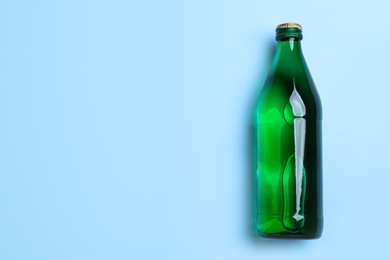 Photo of Glass bottle with water on light blue background, top view. Space for text
