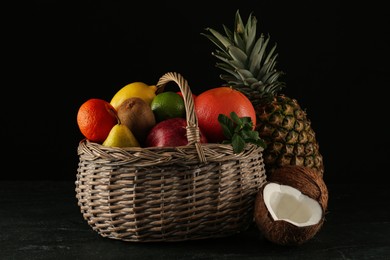 Photo of Fresh ripe fruits and wicker basket on black table