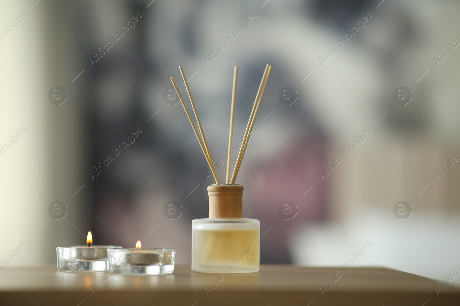 Photo of Aromatic reed air freshener and scented candles on table indoors