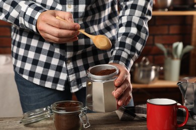 Photo of Man putting ground coffee into moka pot at table in kitchen, closeup