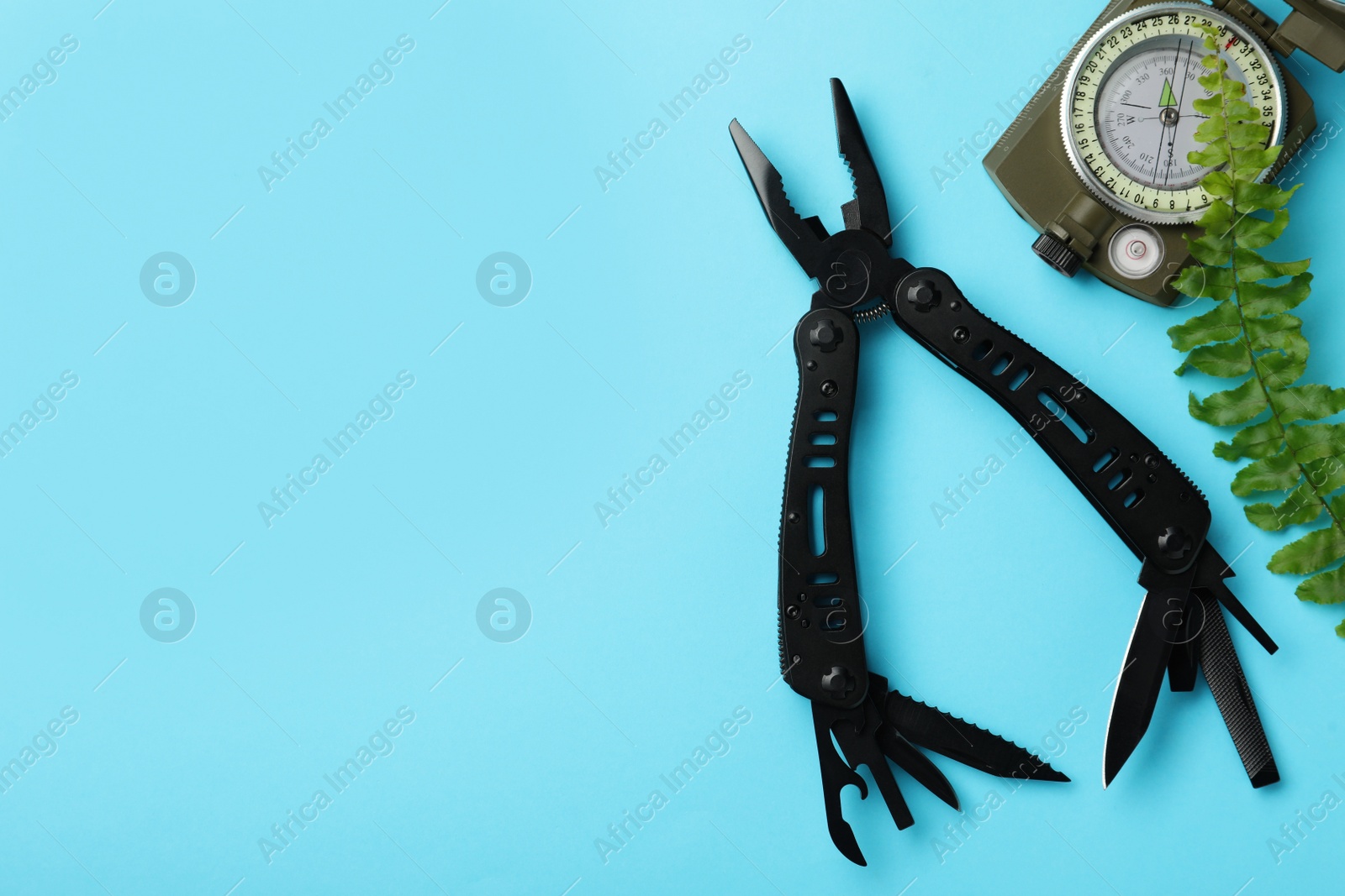 Photo of Compact portable multitool, compass and green leaf on light blue background, flat lay. Space for text