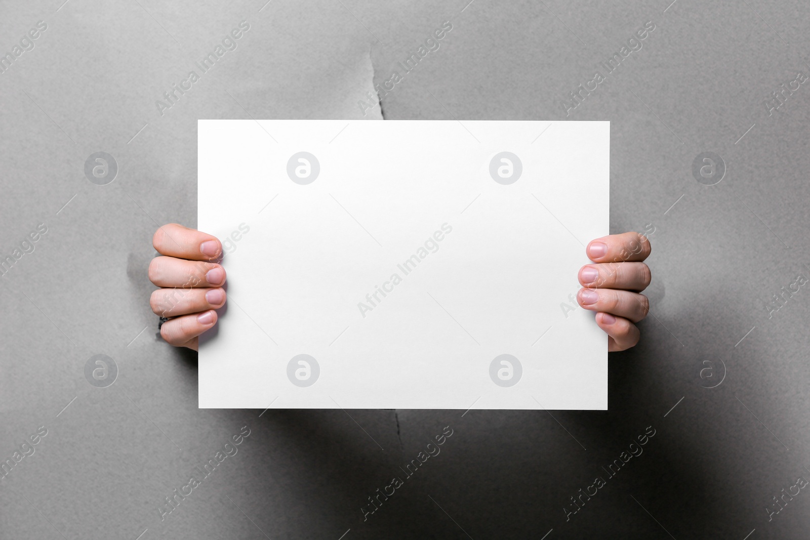 Photo of Man holding sheet of paper through hole in white paper, closeup. Mockup for design