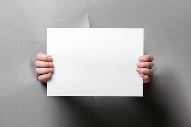 Man holding sheet of paper through hole in white paper, closeup. Mockup for design