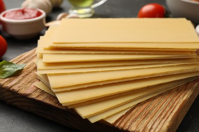 Photo of Cooking lasagna. Wooden board with pasta sheets on dark table, closeup