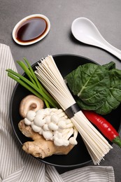 Photo of Cooking delicious ramen soup. Different ingredients in bowls and spoon on gray table, flat lay