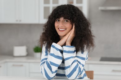 Portrait of beautiful woman with curly hair in kitchen. Attractive lady smiling and looking into camera