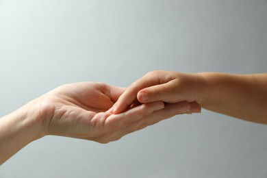 Mother and child holding hands on light blue background, closeup