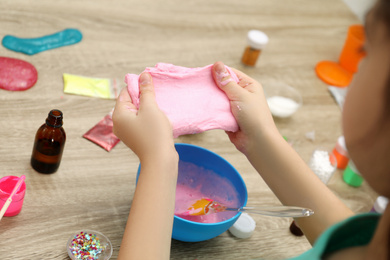 Photo of Little girl making DIY slime toy at table, closeup