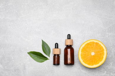 Photo of Bottles of essential oil with orange slice and leaves on grey table, flat lay
