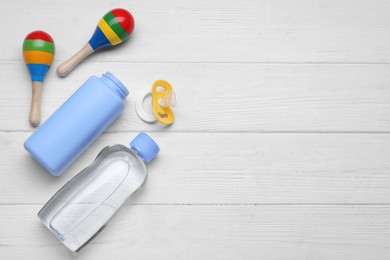 Photo of Baby powder, oil, pacifier and toys on white wooden table, flat lay. Space for text