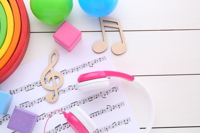 Notes, music sheet, headphones and toys on white wooden table, flat lay with space for text. Baby song concept