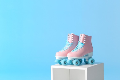 Pair of vintage roller skates on storage cube against color background. Space for text