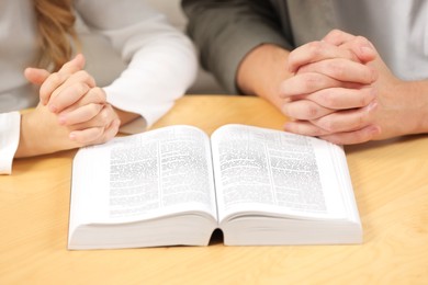 Photo of Girl and her godparent praying over Bible together at table indoors, closeup