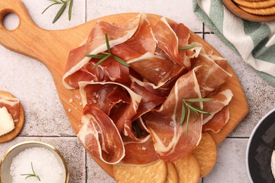 Photo of Slices of tasty cured ham and rosemary on tiled table, flat lay