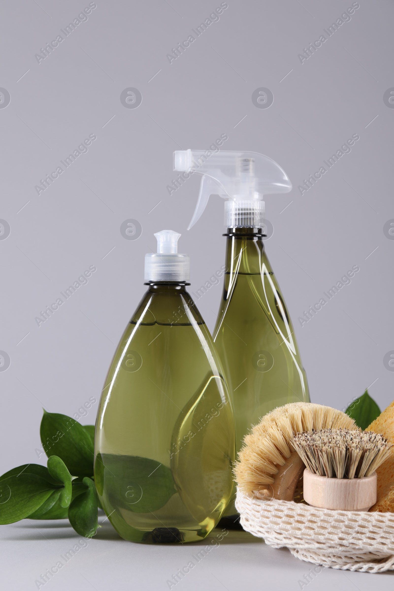 Photo of Bottles of cleaning product, brushes and floral decor on light background