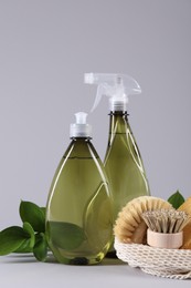 Bottles of cleaning product, brushes and floral decor on light background