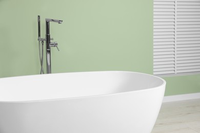 Modern ceramic tub near light green wall in bathroom, closeup. Interior design
