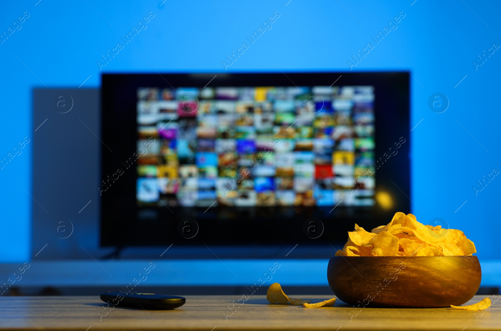 Photo of Bowl of chips and TV remote control on table indoors. Space for text