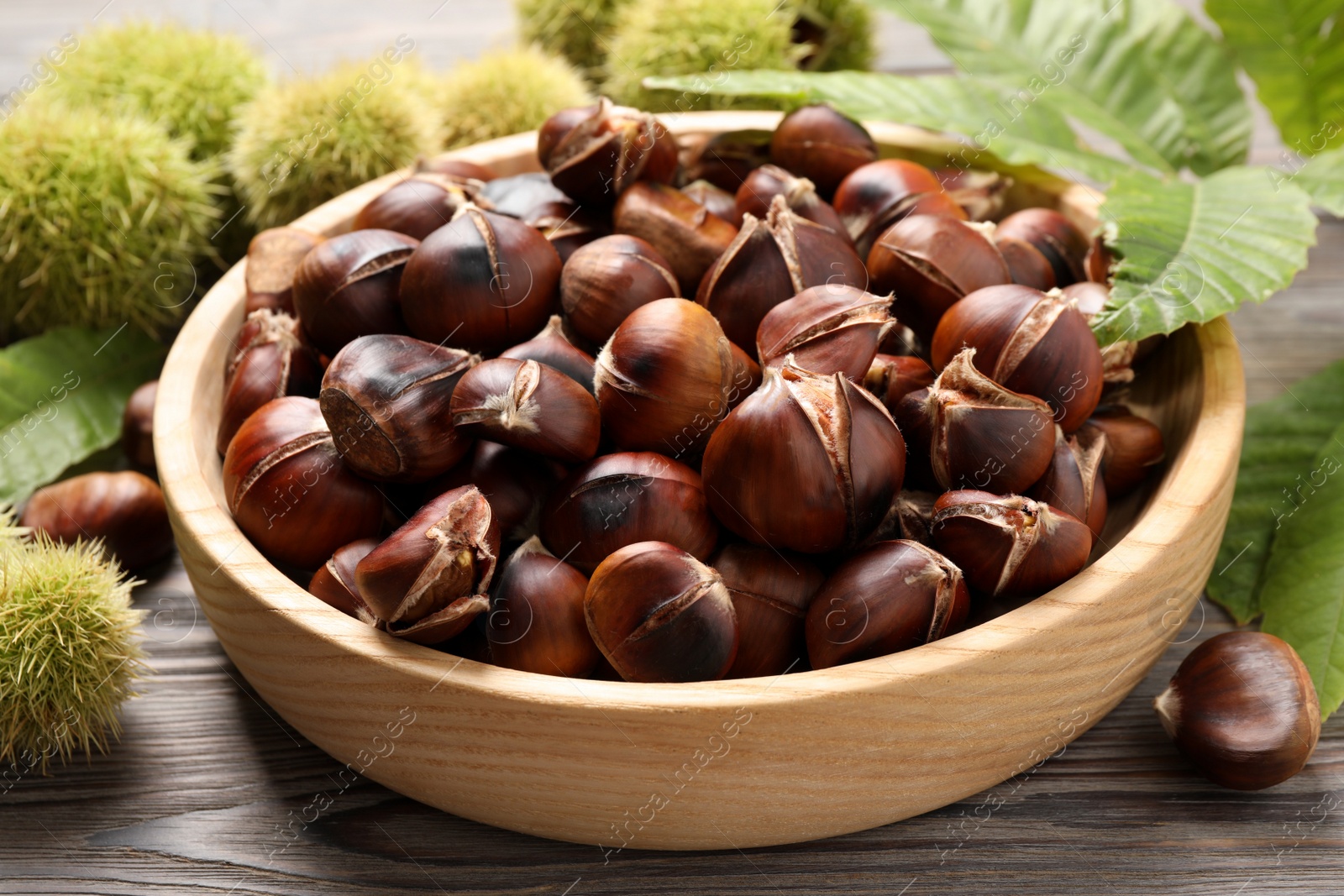 Photo of Delicious roasted edible chestnuts in wooden bowl on table, closeup