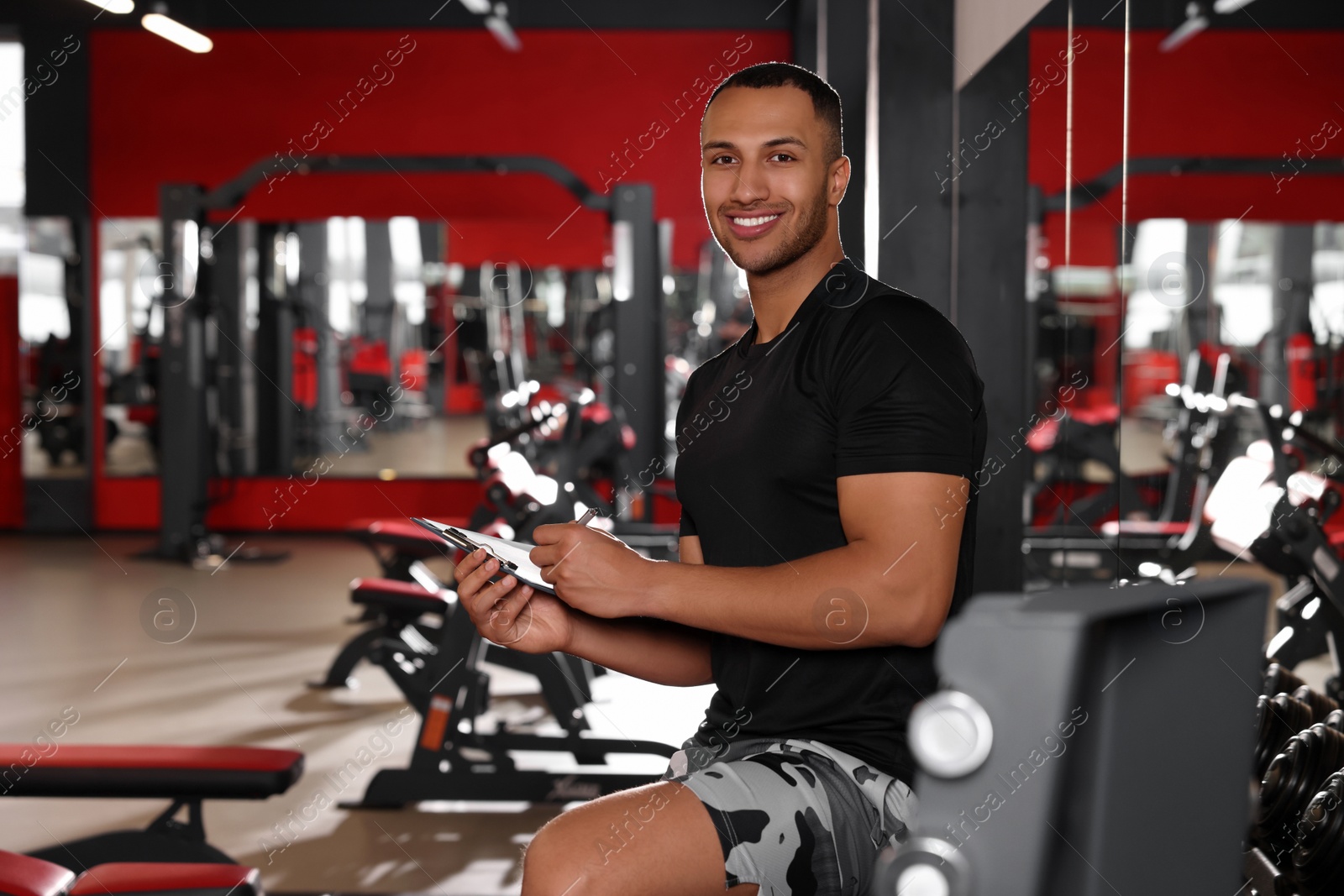 Photo of Happy trainer writing down workout plan in modern gym, space for text