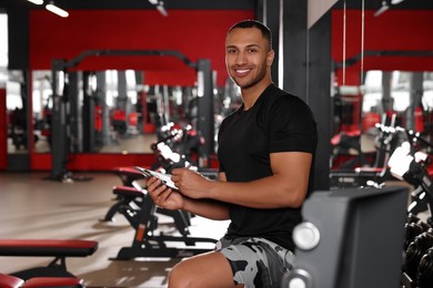 Photo of Happy trainer writing down workout plan in modern gym, space for text