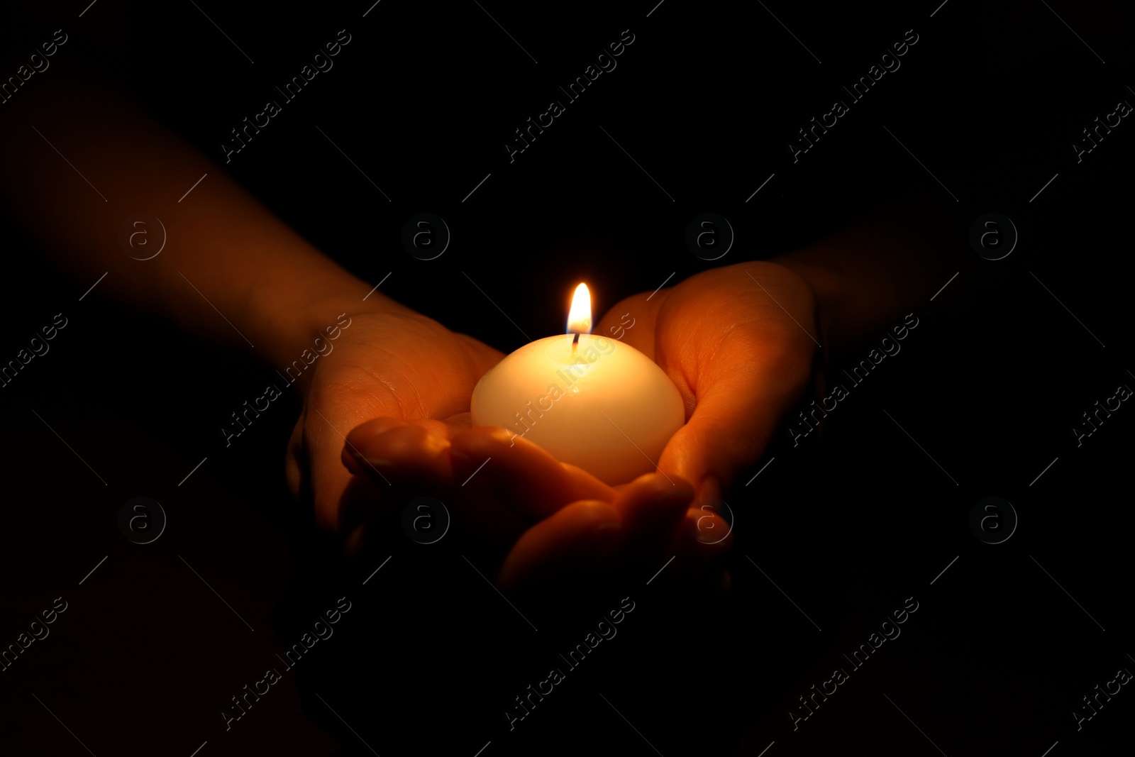 Photo of Woman holding burning candle in hands on black background, closeup