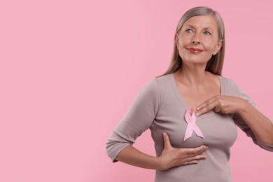 Beautiful senior woman with pink ribbon on color background, space for text. Breast cancer awareness